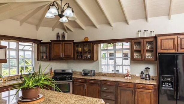 Une cuisine avec des meubles en bois, des plans de travail en granit, un réfrigérateur noir et un ventilateur de plafond.