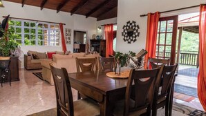 Un espace repas comprenant une table et des chaises en bois, un canapé et une vue sur l’extérieur grâce à de grandes fenêtres.