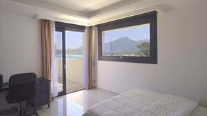 Un dormitorio con cama, escritorio y silla. Se ve una ventana grande con vistas a la montaña.