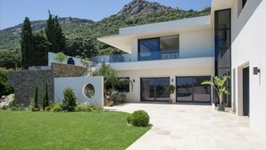 Una casa moderna de dos pisos con fachada de piedra, ventanas amplias y un jardín cuidado.
