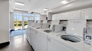 A laundry facility with multiple washing machines and dryers, a blue mat on the floor, and a view of the outside through large windows. - 🚴 Tour de Nash Weekend! Riverfront Condo – on Bike Route + Bike Racks (Nashville)
