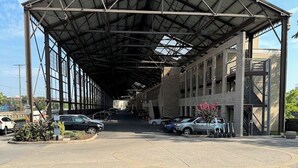 A covered parking area with a metal roof, multiple cars parked, and a building with a brick facade in the background. - 🚴 Tour de Nash Weekend! Riverfront Condo – on Bike Route + Bike Racks (Nashville)