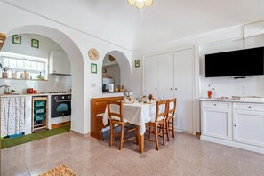 A kitchen with an oven, a dining table with chairs, a TV, and a window.