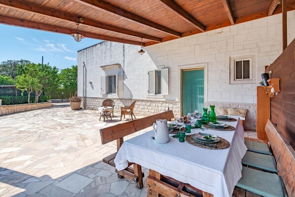 An outdoor dining area with a table set for four, benches, and a brick building in the background.