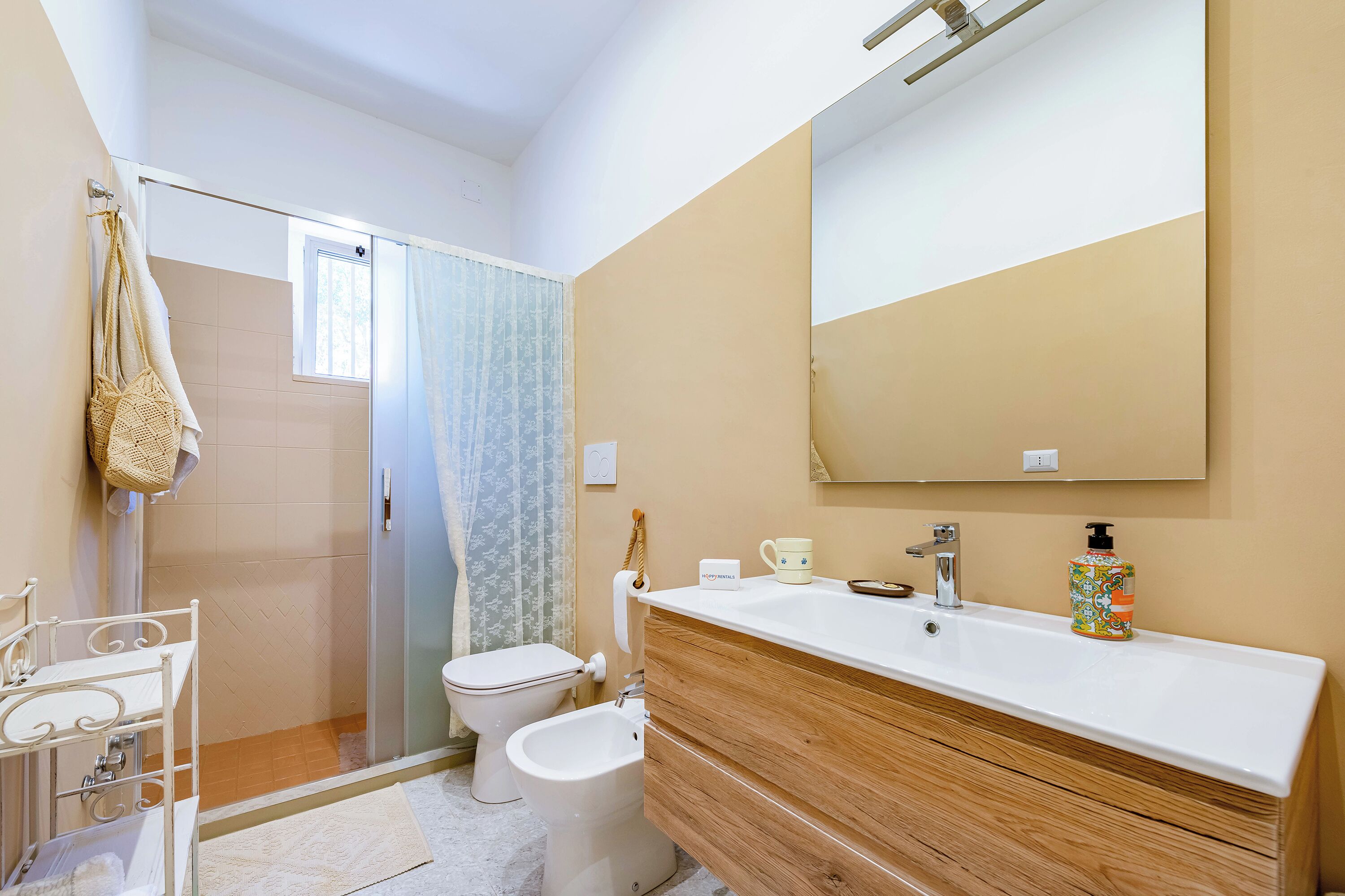A bathroom with a shower, toilet, bidet, vanity with a mirror, and a sink.