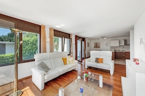 A modern living room with two white sofas, a coffee table, and a view of the kitchen.