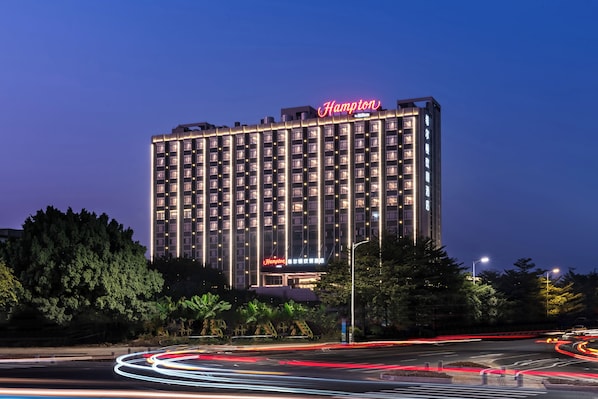 A multi-story hotel with a prominent "Hampton" sign, surrounded by trees and featuring a modern architectural design. - Hampton By Hilton Dongguan Machong (Dongguan)