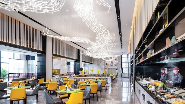 Zona pranzo moderna con sedie gialle, un buffet e un grande lampadario.
