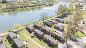 Ein Ufergrundstück mit modernen Blockhäusern, einem Fluss und einer hügeligen Landschaft im Hintergrund.