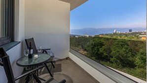 A balcony with a table and chairs, a bottle of wine, and two glasses. The balcony overlooks a cityscape with buildings and trees. - Apt One Kostrena Sea-View Balcony & Parking, Kostrena, Croatia (Kostrena)