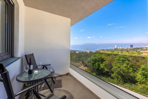 A balcony with a table, two chairs, a wine bottle, and a glass.