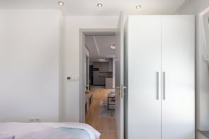 A bedroom with a bed, a wardrobe, and a view into a kitchen area.
