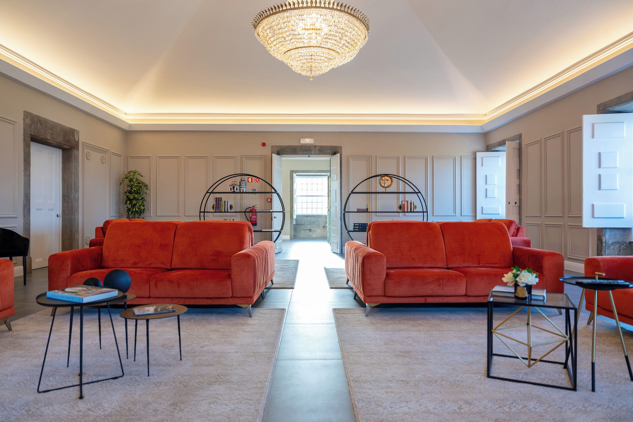 A spacious living room with two red sofas, a chandelier, and a bookshelf.