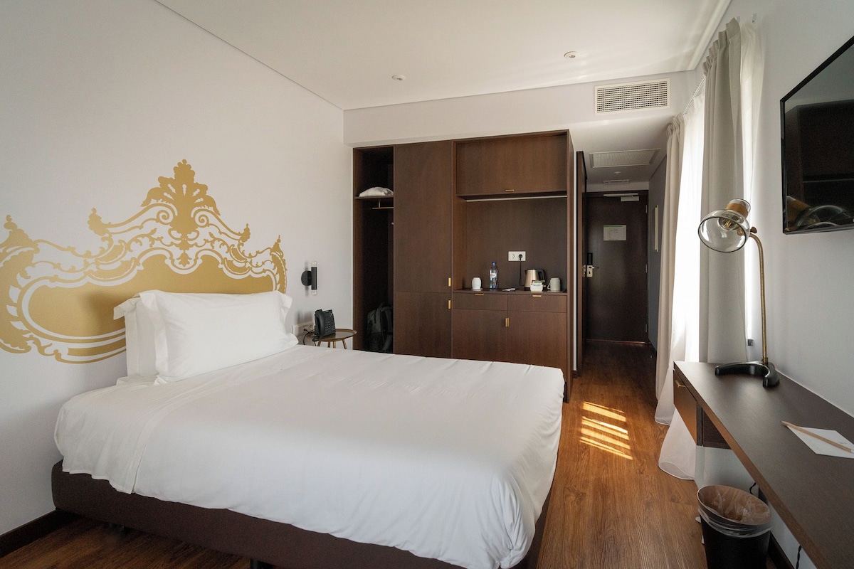 Hotellihuone, jossa on suuri sänky, vaatekaappi, työpöytä lampun kanssa ja peili.