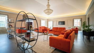 A spacious living room with a large sectional sofa, a decorative metal shelving unit, and a chandelier.