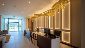A modern reception area with a glass door leading outside, a reception desk with chairs, and a decorative light fixture above. - Palácio Santa Catarina (Angra do Heroismo)
