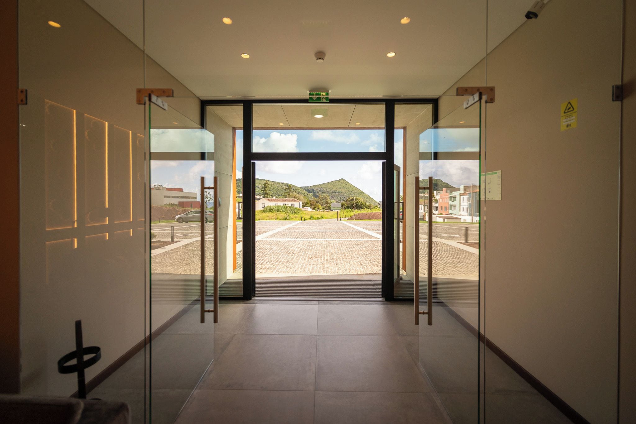 Entrada de hotel con puerta de cristal, suelo de baldosas y vistas a un estacionamiento y edificios.