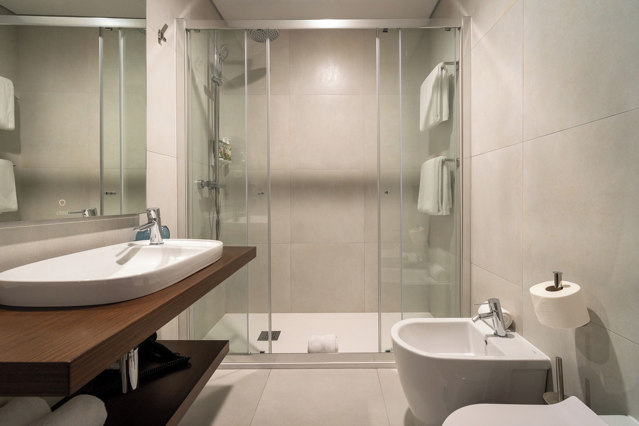 Un baño moderno con ducha envuelta en vidrio, lavamanos, un bidé y un inodoro.