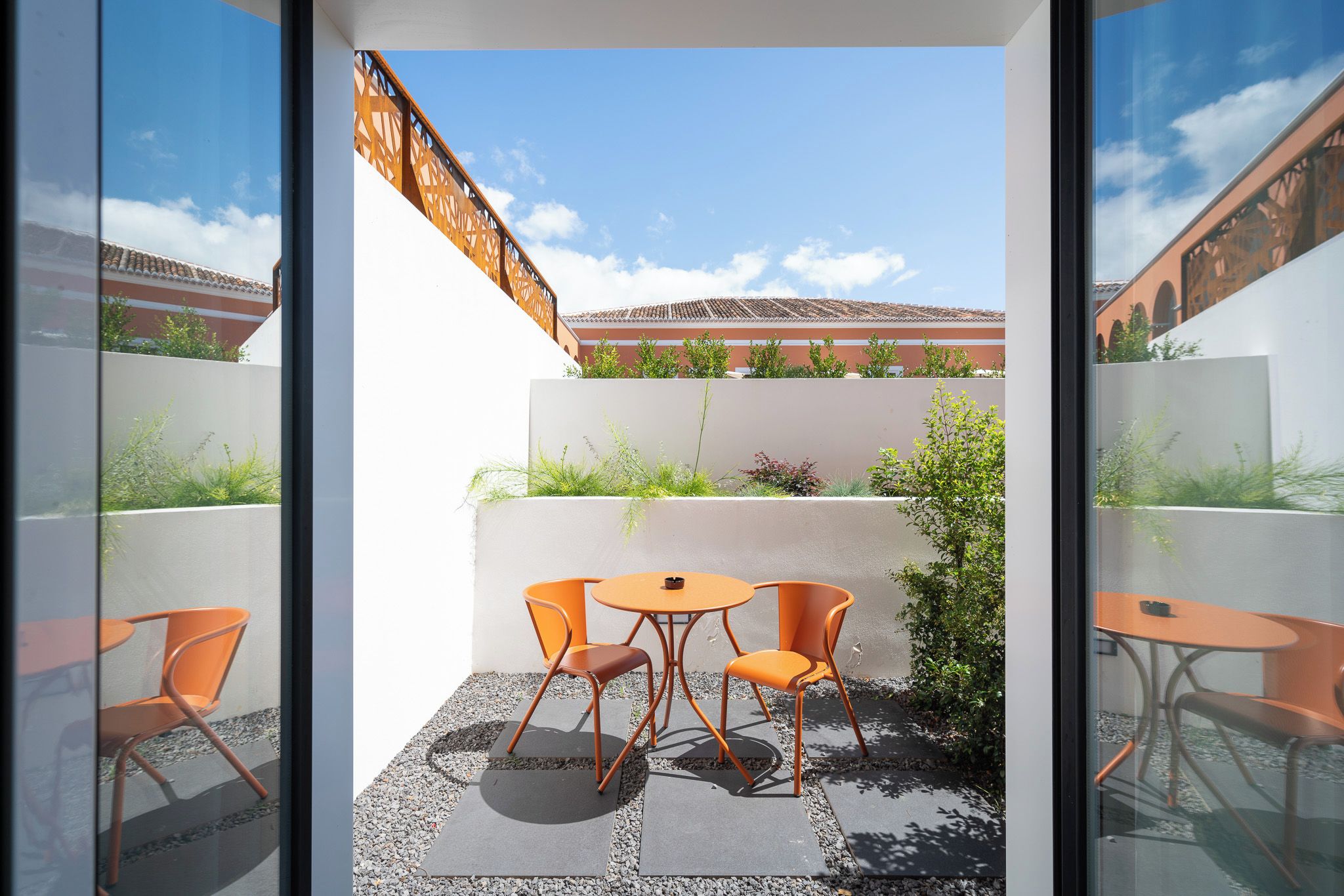 A modern outdoor patio with a table and chairs, a view of a building with a tiled roof, and a clear sky.