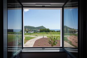 A window with a view of a landscaped area, a pathway, and distant hills. - Palácio Santa Catarina (Angra do Heroismo)