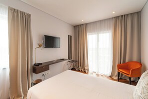 A hotel room with a bed, a desk with a flat-screen TV, a chair, and large windows with curtains. - Palácio Santa Catarina (Angra do Heroismo)