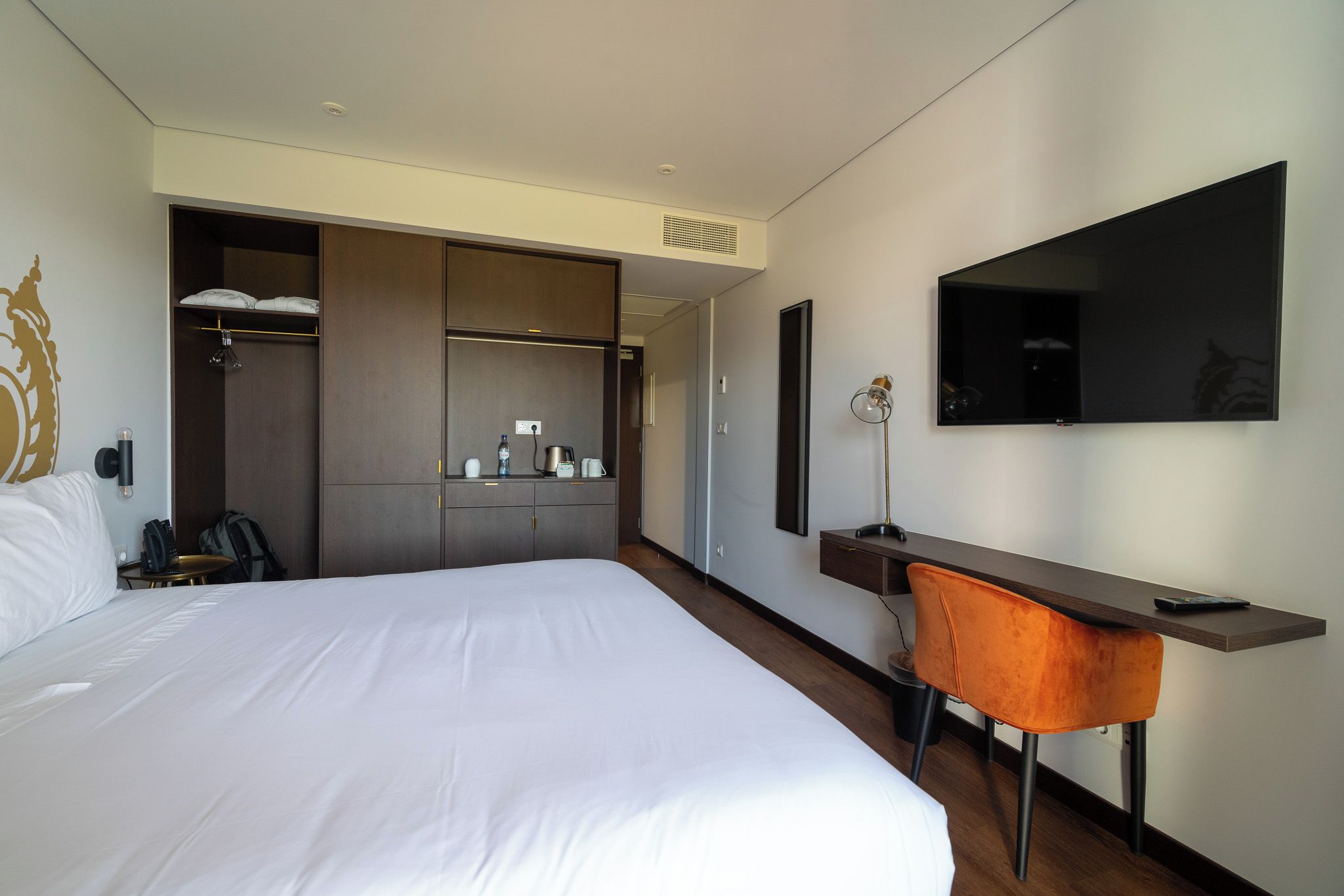 A hotel room with a large bed, a desk with a chair, a television, and a wardrobe.