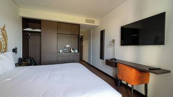 A hotel room with a large bed, a desk with a chair, a television, and a wardrobe.