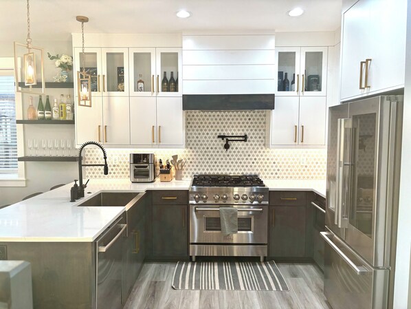 A modern kitchen with stainless steel appliances, white cabinetry, and a patterned backsplash. - Charming house with Beautiful Sunset View (Dallas)