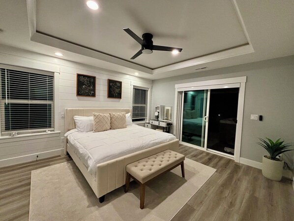 A bedroom with a bed, bench, ceiling fan, and large windows.