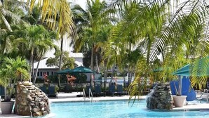 Un área de piscina con palmeras, sillones de descanso y un elemento decorativo de piedra.