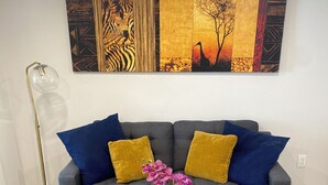 A living room with a grey sofa, blue and mustard pillows, a glass coffee table with a plant, and a floor lamp. - Modern & Elegant One-Bedroom in NoMa, DC (Washington)