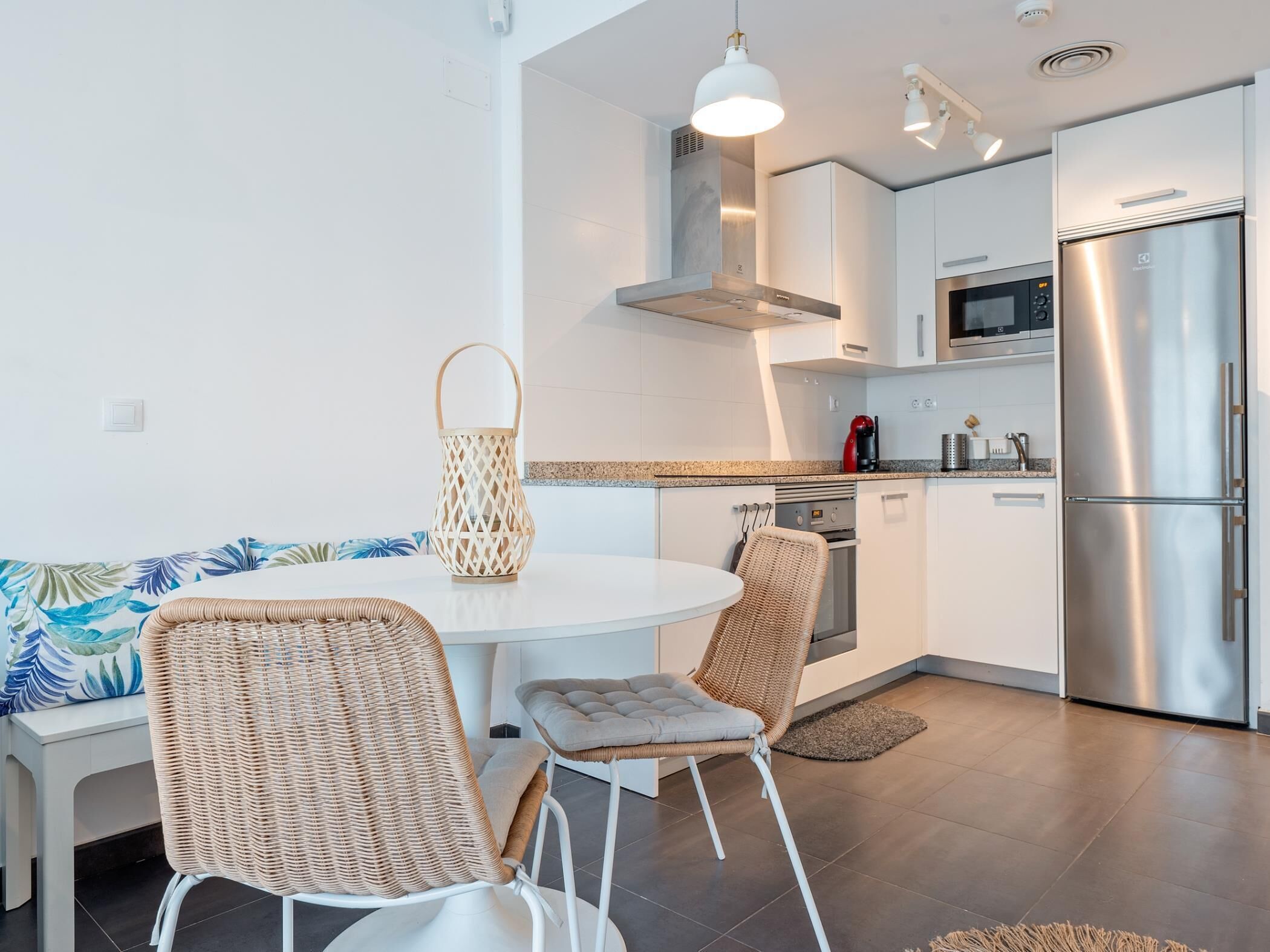 A modern kitchen with white cabinets, stainless steel appliances, and a round dining table with wicker chairs.
