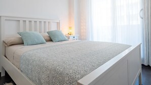 Un letto rifatto con una coperta a motivi, un comodino con una lampada e tende leggere su una finestra.