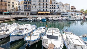 Un port de plaisance où sont amarrés différents types de bateaux, entouré d’immeubles à plusieurs étages dotés de balcons et de boutiques.
