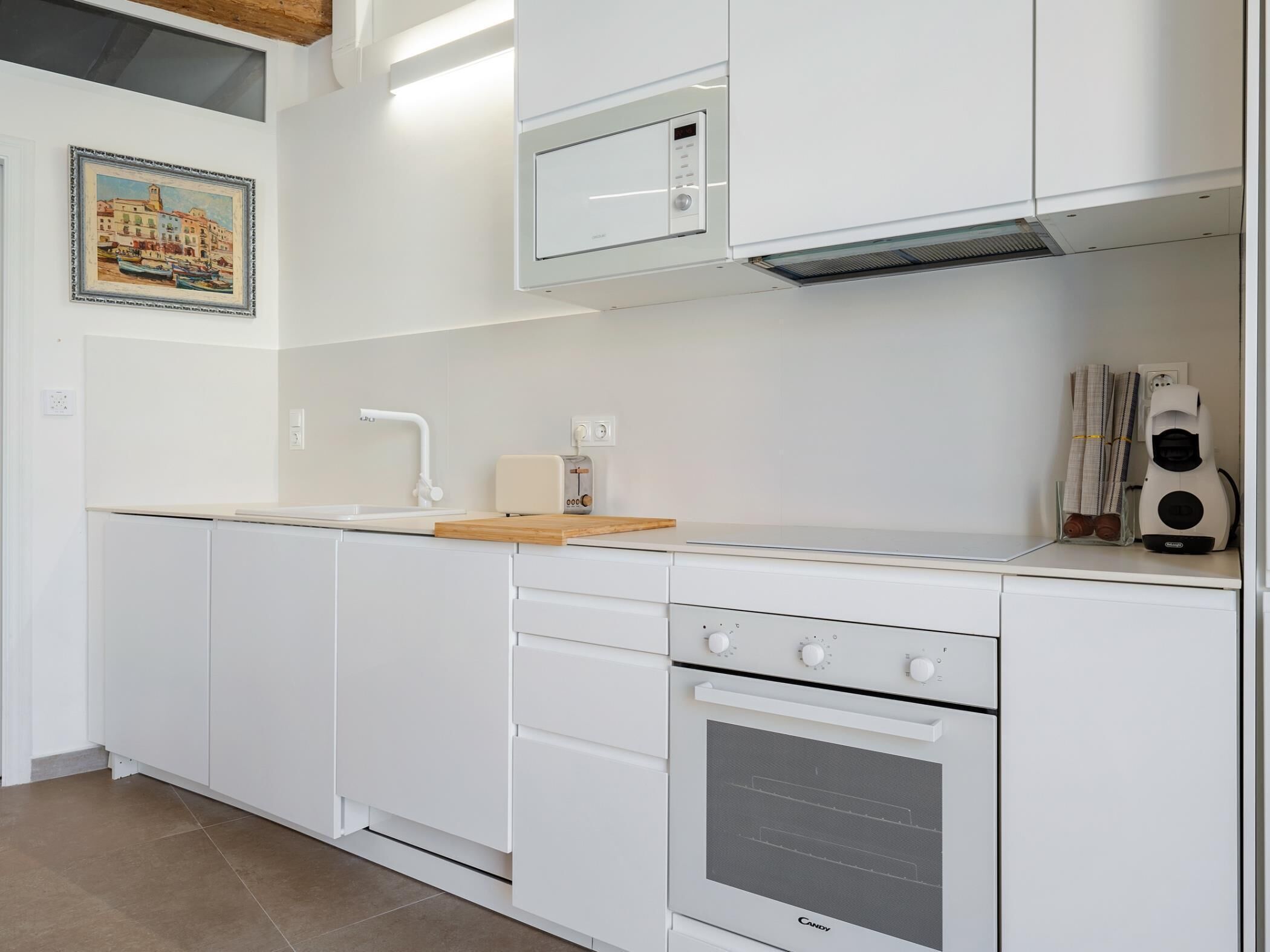 Une cuisine moderne avec des meubles blancs, un four encastré, un four à micro-ondes et un grille-pain.