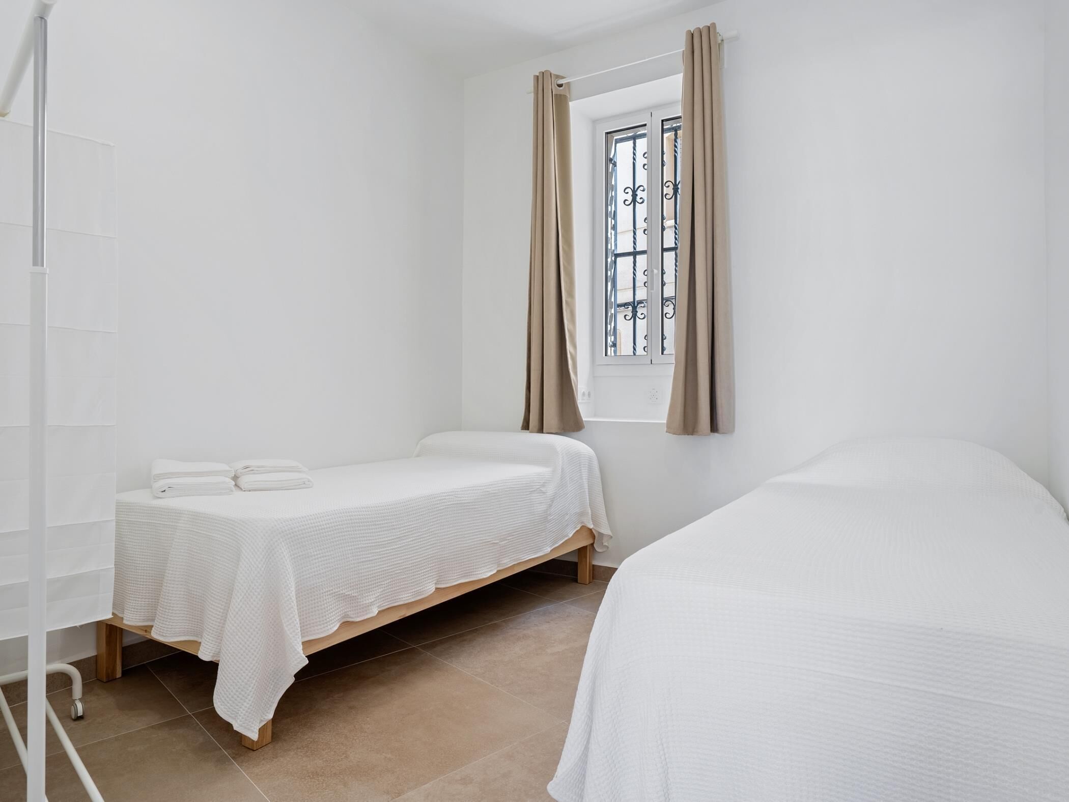 Una habitación pequeña y limpia con dos camas individuales, una ventana con cortinas y un radiador blanco.