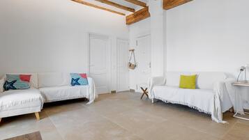 Un amplio salón con dos sofás blancos, vigas de madera en el techo y suelo de baldosas.