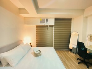 Habitación de hotel con cama, escritorio, silla, lámpara y ventana con persianas.