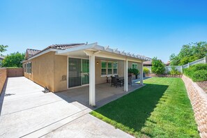 Ein Haus mit überdachter Terrasse, Rasen und einer Ziegelmauer.