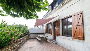 Ein Patio mit Backsteinboden, Holzbanken und einem großen Sonnenschirm, der Schatten spendet.