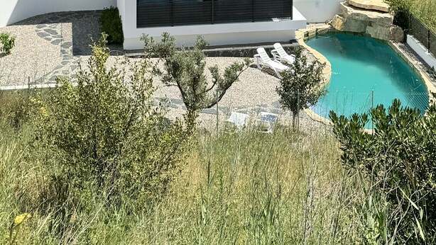 A modern two-story house with large glass windows, a pool, and a stone wall.