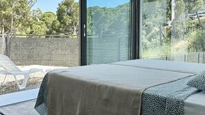 A modern bedroom with a large bed, a view of the outdoors, and a wooden floor.