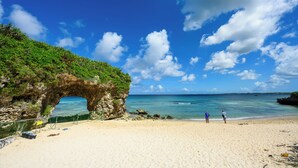 A beach with a natural rock arch, clear blue sky, and calm sea.