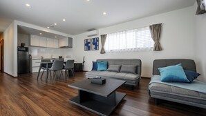 A modern living room with a grey sofa, a coffee table, and a dining area with chairs and a kitchen in the background.