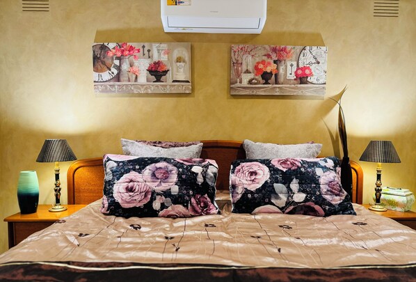A bedroom with a bed, two nightstands, two lamps, and two wall-mounted paintings.