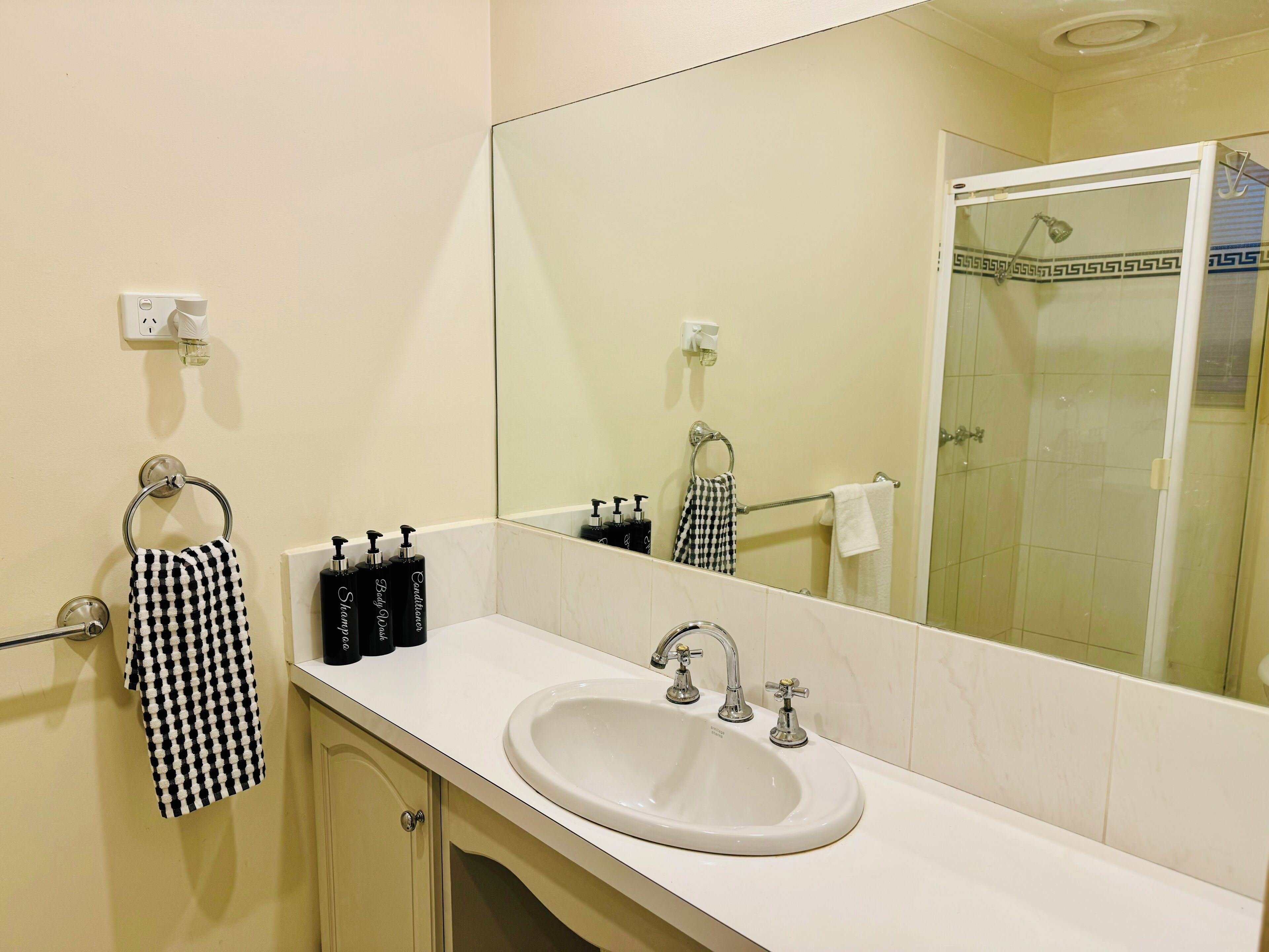 A bathroom with a white sink, a large mirror, and a shower area.