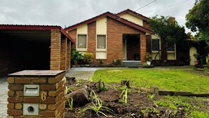 Une maison à deux étages, construite en briques, avec un garage, une petite cour devant avec de jeunes plantes et une boîte aux lettres portant le numéro 6.