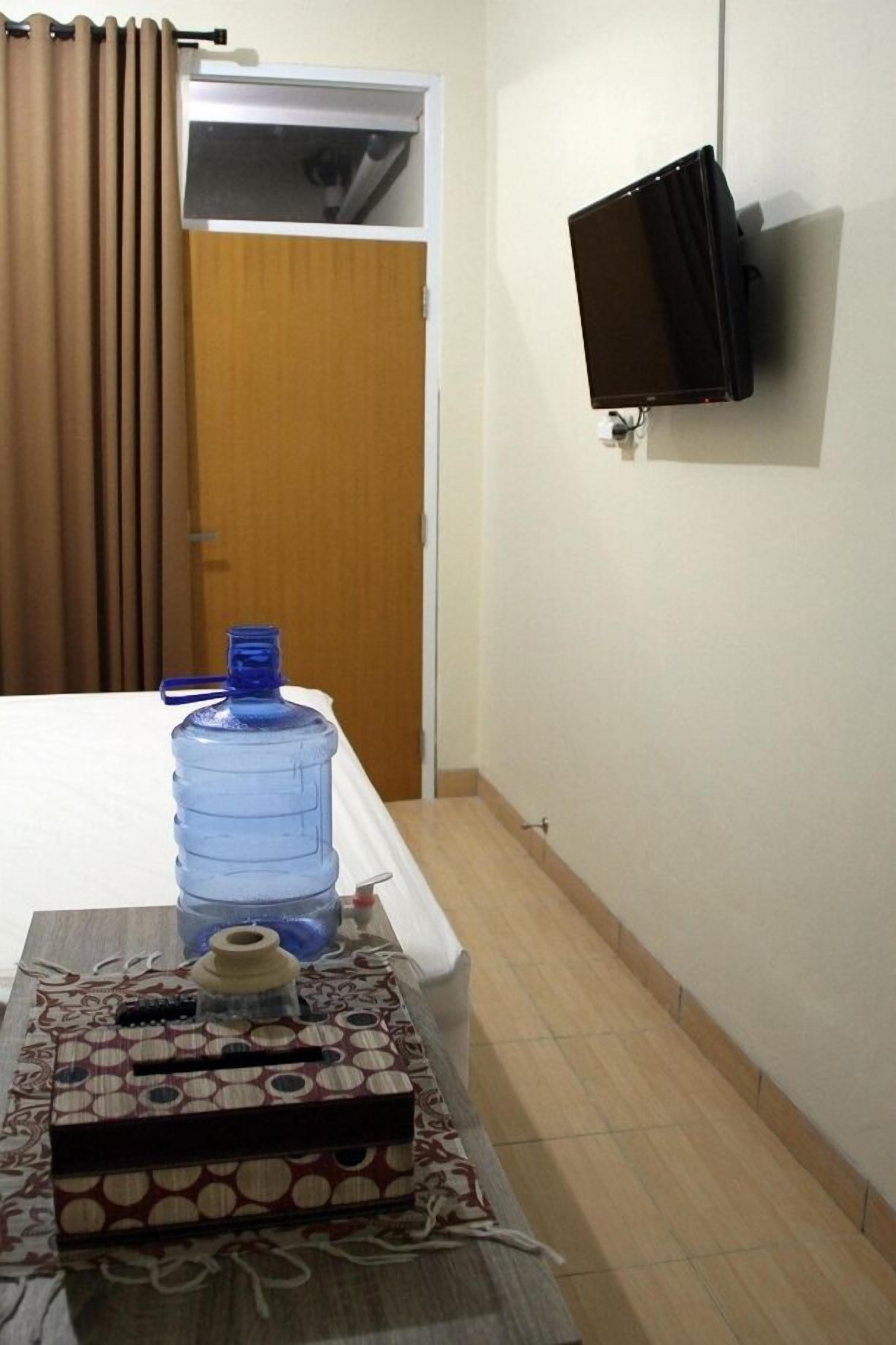 Habitación de hotel con cama, un dispensador grande de agua, televisor montado en la pared y una puerta con cortinas.