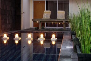 A pool area with a bench and chairs, surrounded by potted plants. - Green Leaf Guest House Jogja by Sinergi (Depok)
