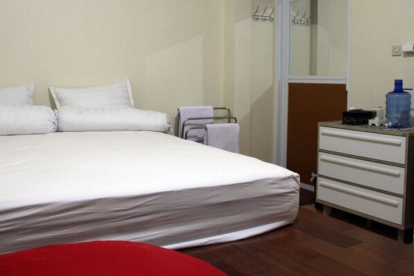 Une chambre d’hôtel avec un grand lit, une commode en bois, une chaise rouge et une bouteille d’eau posée sur la commode.